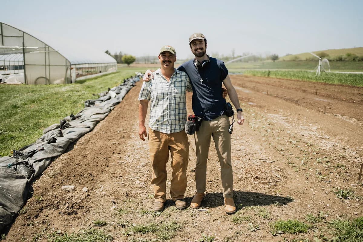 Jack Dempsey with a customer beside a greenhouse and growing beds
